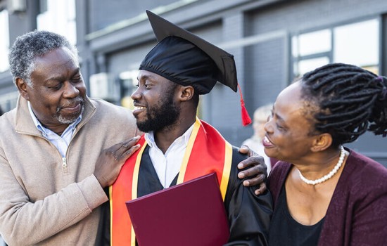A young man in a graduation robe surrounded by his parents.