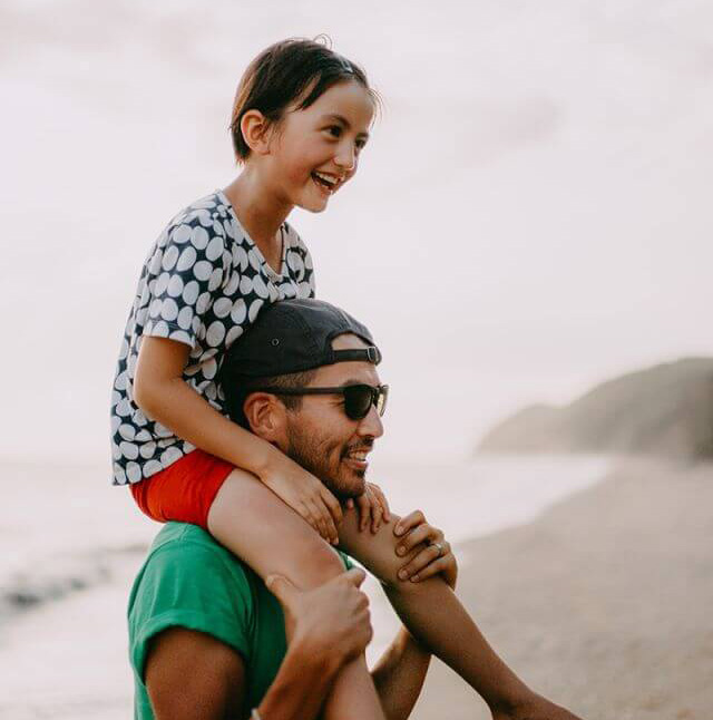 A father carrying his daughter on his shoulders at the beach